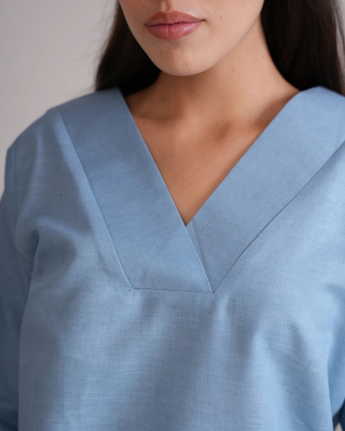 A close-up of a woman wearing a light blue V-neck top or scrub top, showing the fabric texture and collar detail.