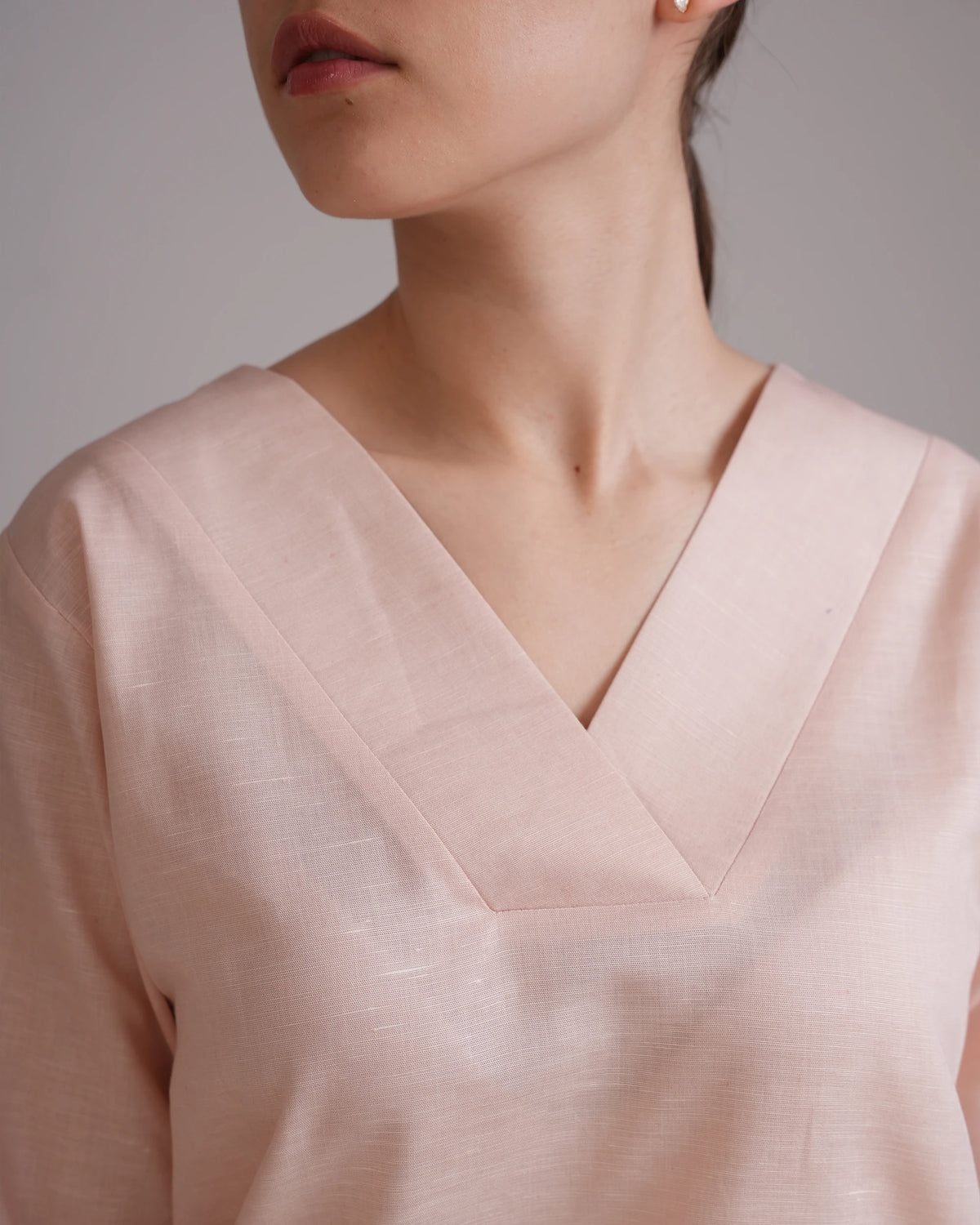 Close-up of a model wearing a pale blush pink V-neck top with a subtle textured linen-like fabric.