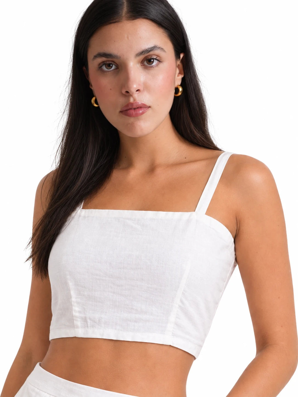 A woman modeling a white cropped camisole top with thin straps and a square neckline against a plain white background.