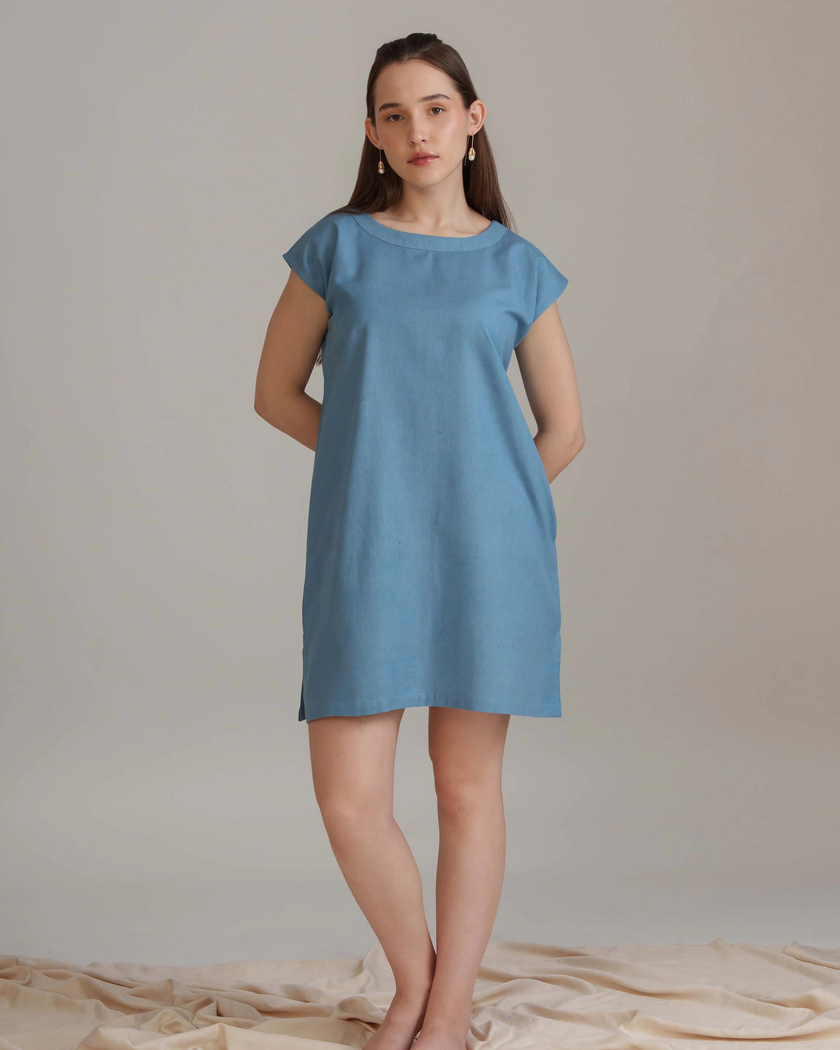 A woman modeling a simple short-sleeve blue dress against a plain beige studio backdrop.