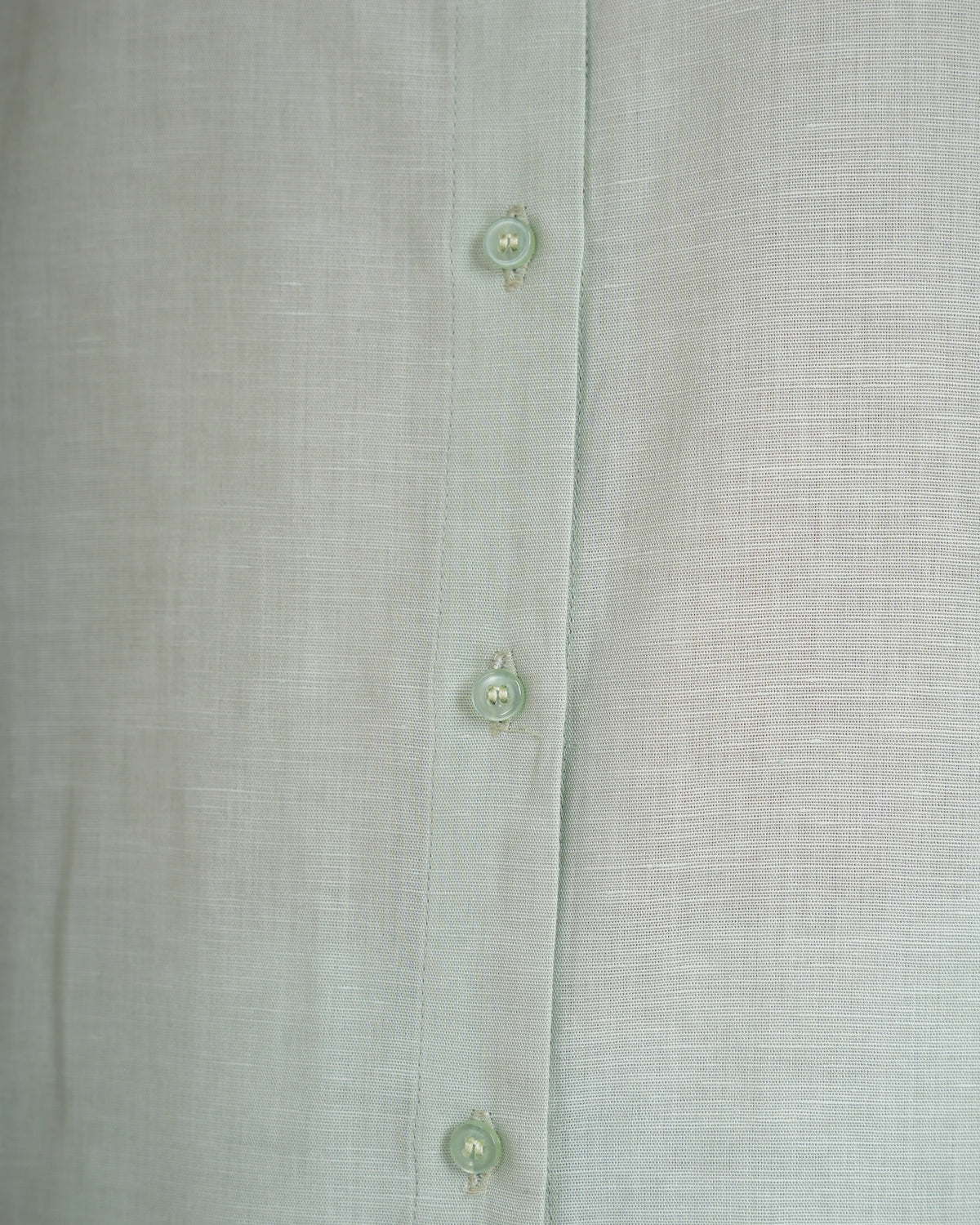 Close-up of a light sage green linen button-up shirt showing the fabric texture and three matching buttons.