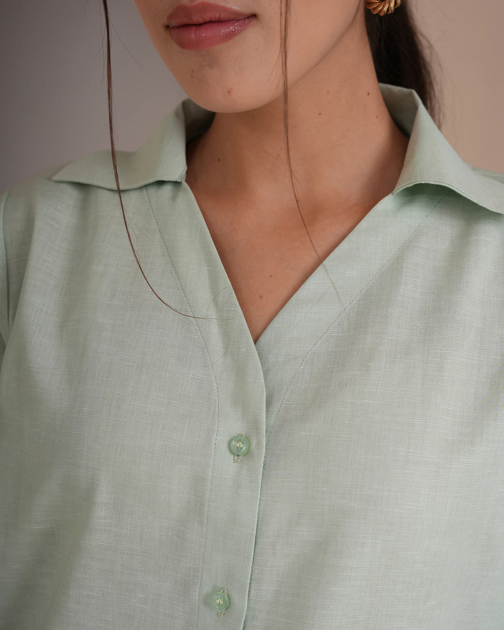 Close-up of a woman wearing a pale sage green linen button-up shirt with a collar and matching buttons.